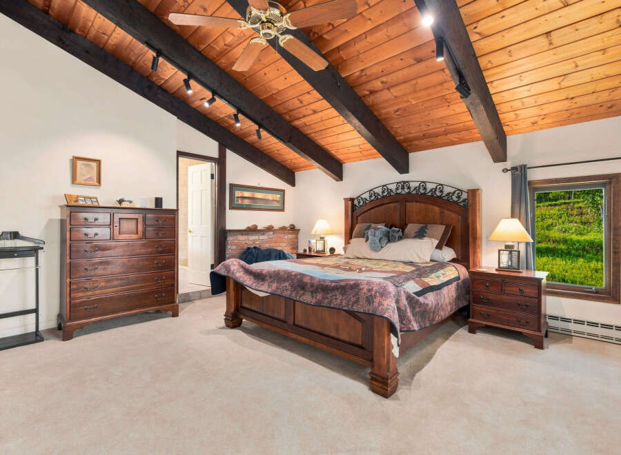 Experience rustic charm in this spacious bedroom featuring a vaulted wood-beamed ceiling and a cozy brick fireplace.