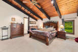 Experience rustic charm in this spacious bedroom featuring a vaulted wood-beamed ceiling and a cozy brick fireplace.
