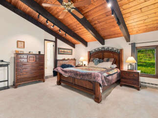Experience rustic charm in this spacious bedroom featuring a vaulted wood-beamed ceiling and a cozy brick fireplace.