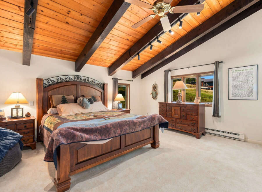 Experience rustic charm in this inviting bedroom, featuring a grand wooden bed with a decorative headboard and a cozy, patterned quilt.