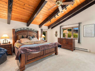 Experience rustic charm in this inviting bedroom, featuring a grand wooden bed with a decorative headboard and a cozy, patterned quilt.