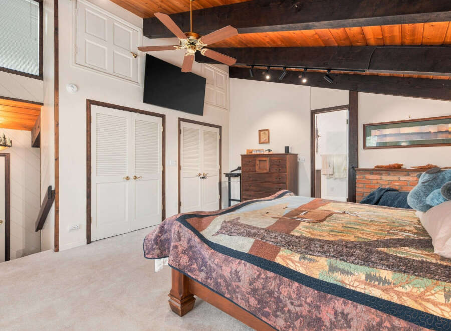 Experience rustic charm in this inviting bedroom featuring a cozy quilt-adorned bed and a warm wooden ceiling with exposed beams.