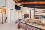 Experience rustic charm in this inviting bedroom featuring a cozy quilt-adorned bed and a warm wooden ceiling with exposed beams.