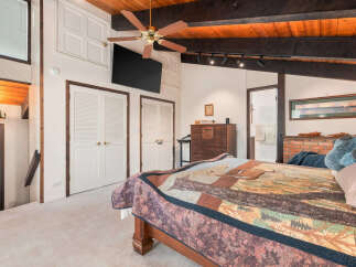 Experience rustic charm in this inviting bedroom featuring a cozy quilt-adorned bed and a warm wooden ceiling with exposed beams.