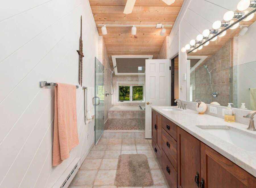 This spacious bathroom features a luxurious soaking tub with a view of the outdoors, a separate glass-enclosed shower, and a double vanity with marble countertops.