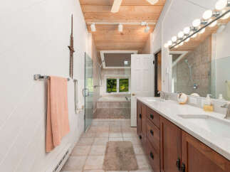 This spacious bathroom features a luxurious soaking tub with a view of the outdoors, a separate glass-enclosed shower, and a double vanity with marble countertops.