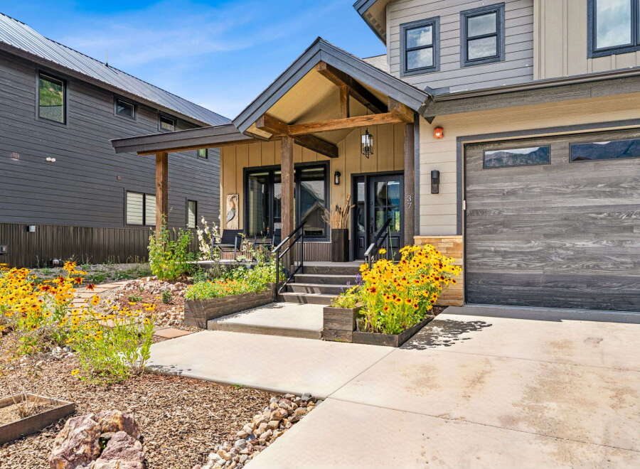 Experience modern mountain living in this stunning home featuring a covered front porch with exposed beams and a cozy seating area.