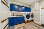 This laundry room boasts stylish navy blue cabinetry with gold hardware, providing ample storage and a modern aesthetic.