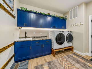 This laundry room boasts stylish navy blue cabinetry with gold hardware, providing ample storage and a modern aesthetic.