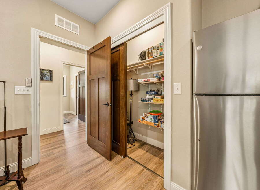 Discover ample storage solutions in this home, featuring a spacious pantry filled with board games and a large stainless steel refrigerator.
