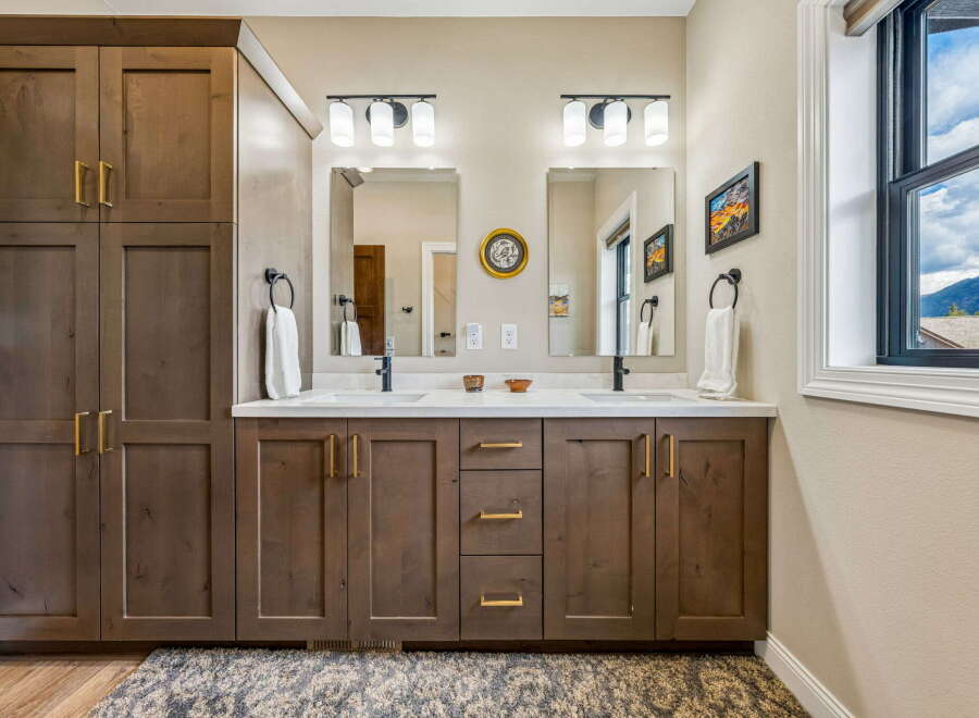 This modern bathroom features a spacious double vanity with ample storage, complemented by sleek gold hardware and a clean white countertop.