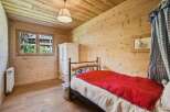 Experience rustic charm in this cozy bedroom, featuring warm wooden walls and ceiling, a comfortable bed with a vibrant red throw, and a charming window overlooking the picturesque surroundings.