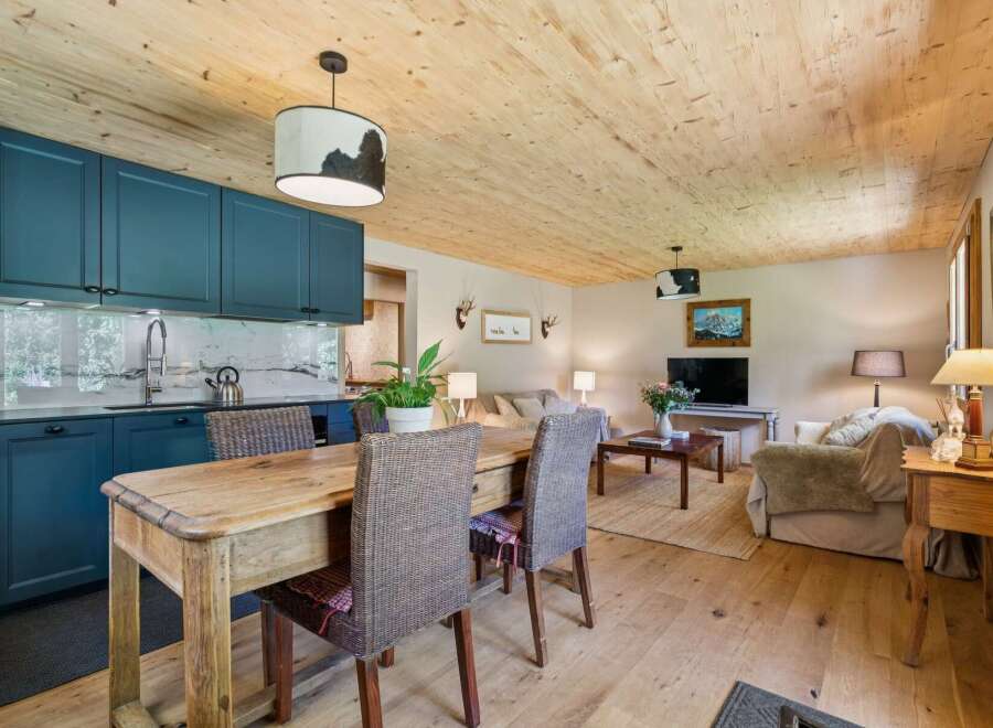 Experience cozy living in this charming open-concept space, featuring a modern kitchen with deep blue cabinetry and a rustic wooden dining table perfect for intimate meals.