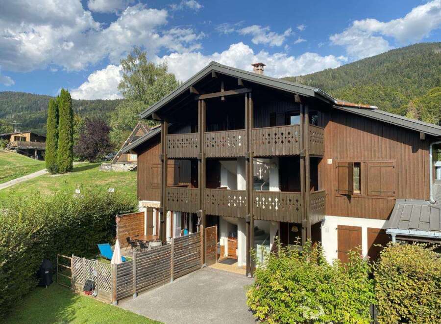 Experience mountain living in this charming wooden chalet, nestled against a backdrop of lush green hills and a clear blue sky.