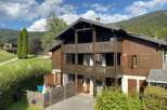 Experience mountain living in this charming wooden chalet, nestled against a backdrop of lush green hills and a clear blue sky.