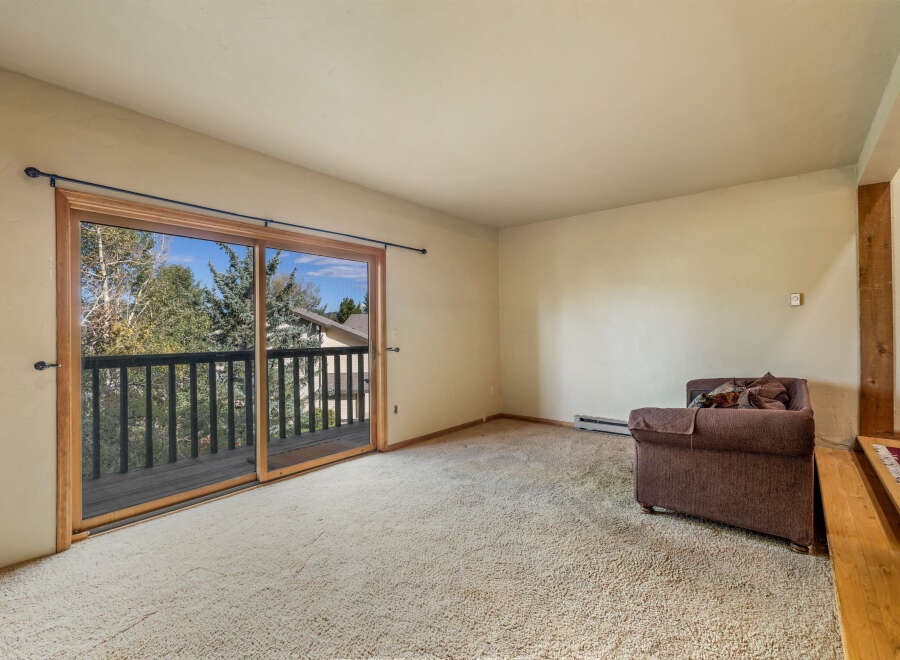 Step out onto the private balcony from this spacious living area, offering serene views of the surrounding trees and sky.