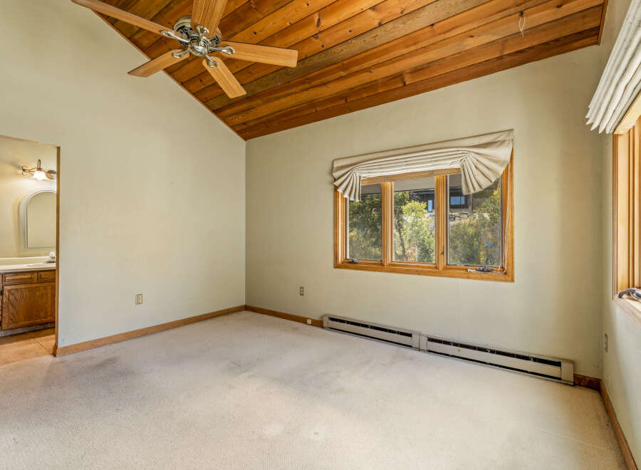 Discover comfort and style in this inviting bedroom featuring a vaulted wood-paneled ceiling with a ceiling fan for optimal air circulation.