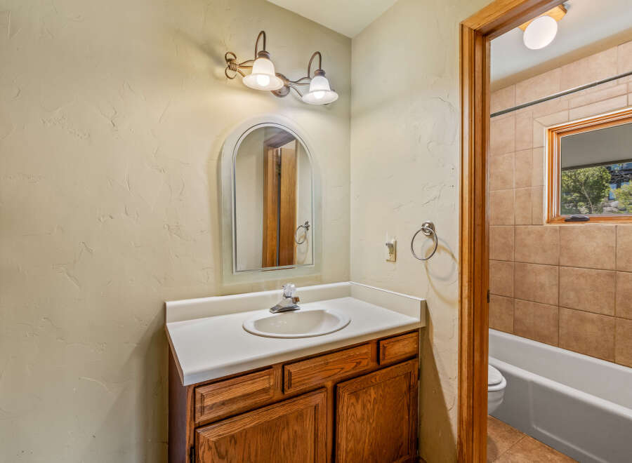 This charming bathroom features a wooden vanity with a white countertop and a sleek faucet, complemented by an arched mirror above.