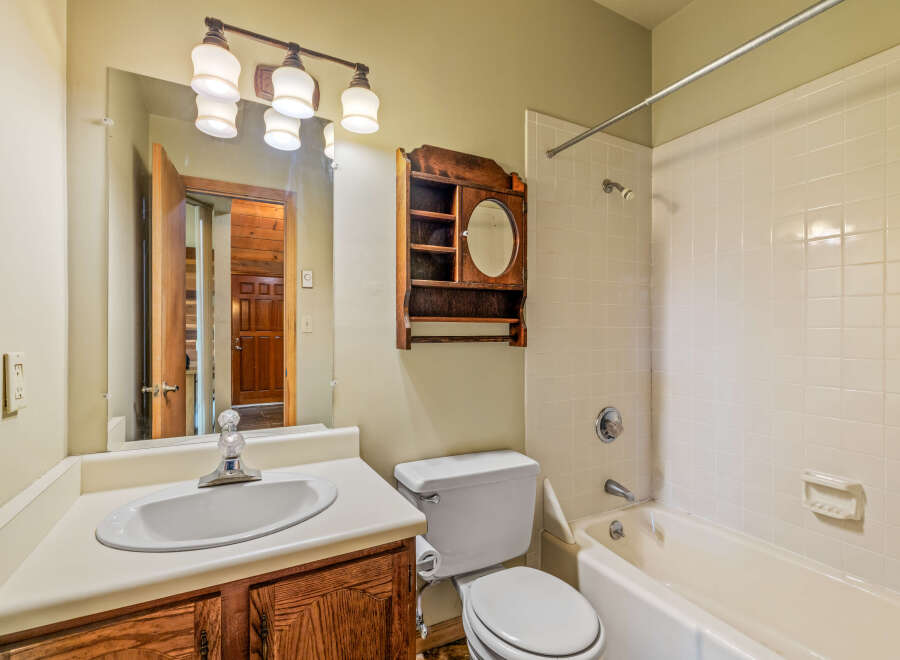 This bathroom features a classic white tub and shower combination with tiled walls, complemented by a wooden vanity with a white sink and a large mirror.