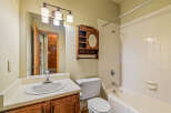 This bathroom features a classic white tub and shower combination with tiled walls, complemented by a wooden vanity with a white sink and a large mirror.