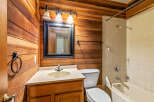 This bathroom features a charming rustic aesthetic with warm wood-paneled walls and a classic white tiled shower/tub combination.