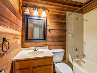This bathroom features a charming rustic aesthetic with warm wood-paneled walls and a classic white tiled shower/tub combination.