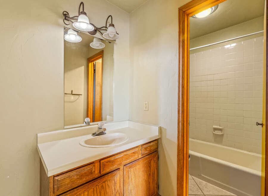 This bathroom features a classic vanity with a white countertop and a wooden cabinet base, complemented by a large mirror with a decorative light fixture above.