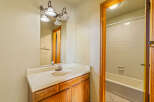 This bathroom features a classic vanity with a white countertop and a wooden cabinet base, complemented by a large mirror with a decorative light fixture above.