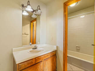 This bathroom features a classic vanity with a white countertop and a wooden cabinet base, complemented by a large mirror with a decorative light fixture above.