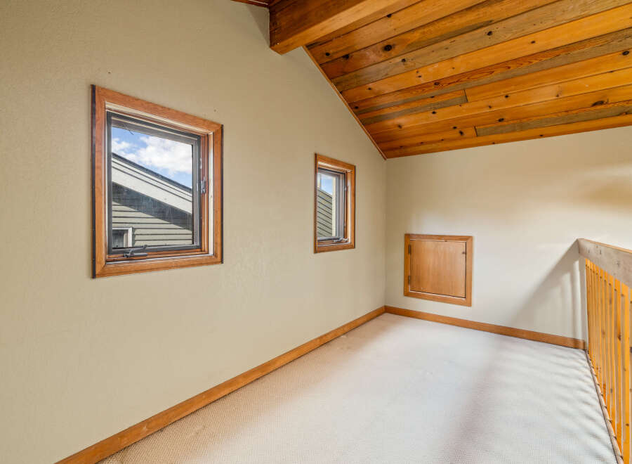 Discover this charming attic space featuring a vaulted wooden ceiling and two inviting windows that offer natural light.