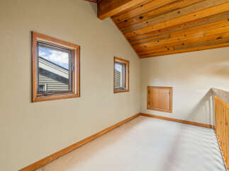 Discover this charming attic space featuring a vaulted wooden ceiling and two inviting windows that offer natural light.