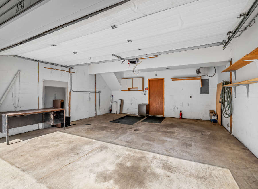 Discover the potential of this spacious garage, featuring a durable concrete floor and ample overhead storage with sturdy wooden shelves.