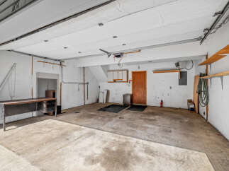Discover the potential of this spacious garage, featuring a durable concrete floor and ample overhead storage with sturdy wooden shelves.