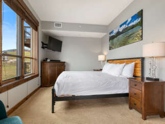 Experience comfort and style in this beautifully appointed bedroom, featuring a plush queen-size bed with crisp white linens and a striking wooden headboard.