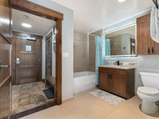 This spacious bathroom features a modern vanity with a granite countertop and a large, illuminated mirror.