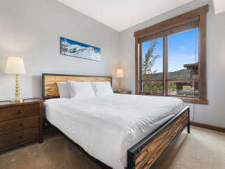 Experience mountain living in this beautifully appointed bedroom featuring a comfortable king-sized bed and a stunning panoramic view of snow-capped peaks through a large window.