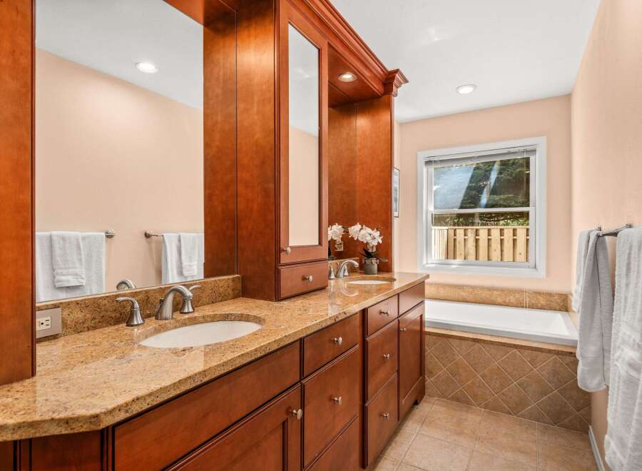 This elegant bathroom features a spacious double vanity with granite countertops and rich cherry wood cabinetry.