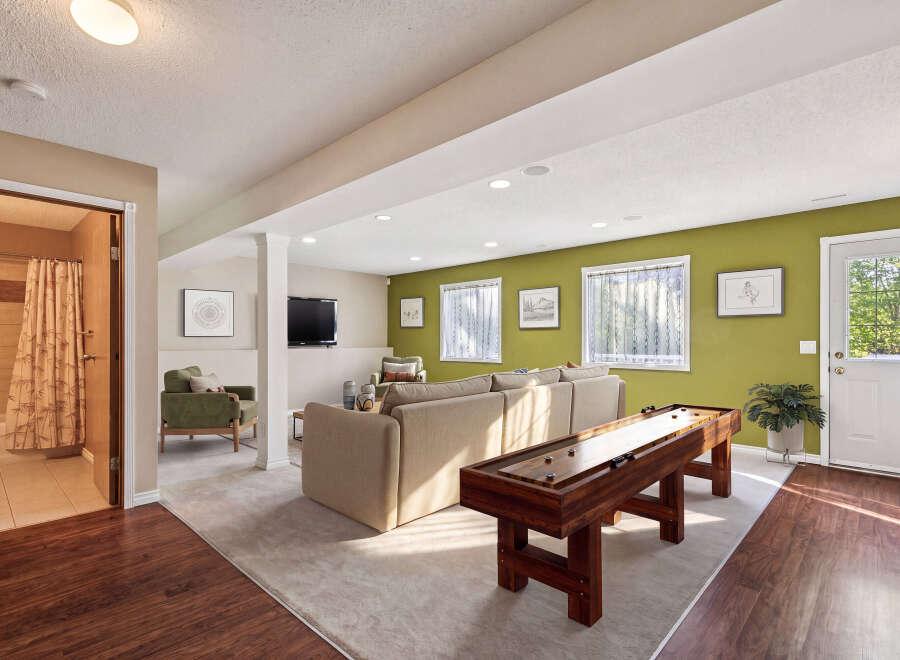 This finished basement offers a perfect blend of relaxation and entertainment, featuring a cozy living area with a large sectional sofa and a dedicated game space with a shuffleboard table.
