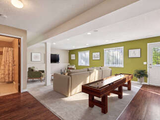 This finished basement offers a perfect blend of relaxation and entertainment, featuring a cozy living area with a large sectional sofa and a dedicated game space with a shuffleboard table.