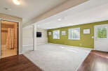 Discover this spacious finished basement featuring a large open living area with plush carpeting and a vibrant accent wall.