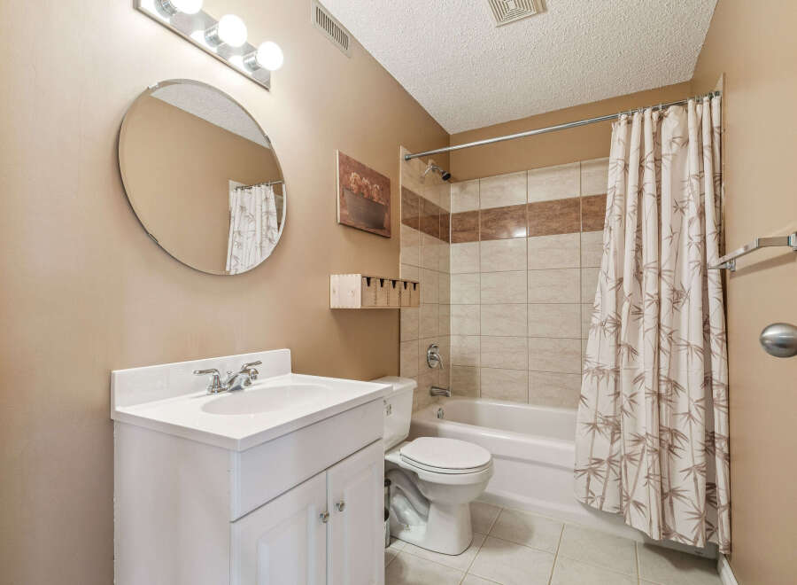 This bathroom features a white vanity with a double-door cabinet, a round mirror, and a vanity light fixture.
