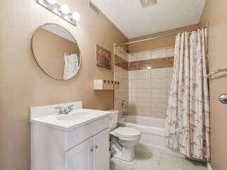 This bathroom features a white vanity with a double-door cabinet, a round mirror, and a vanity light fixture.