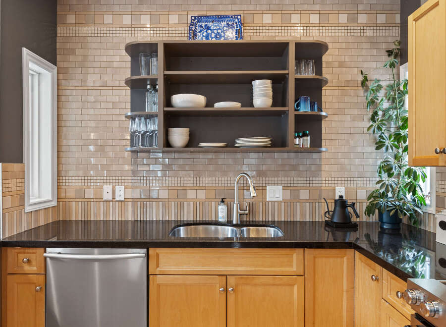 This kitchen boasts a stylish backsplash with a mix of subway and mosaic tiles, complemented by a sleek stainless steel sink and faucet.