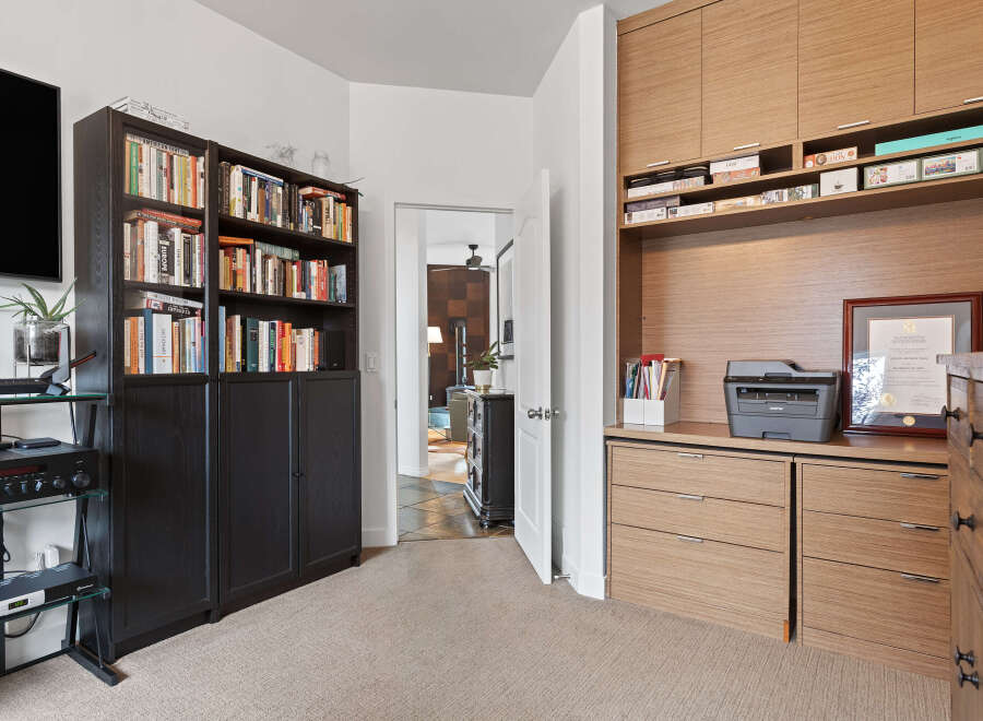 This home office space features a large built-in wooden desk with ample storage, including drawers and shelving.