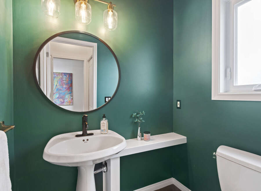 This stylish bathroom features a deep green accent wall, a modern pedestal sink with a dark bronze faucet, and a round mirror.