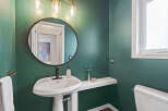 This stylish bathroom features a deep green accent wall, a modern pedestal sink with a dark bronze faucet, and a round mirror.