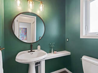 This stylish bathroom features a deep green accent wall, a modern pedestal sink with a dark bronze faucet, and a round mirror.