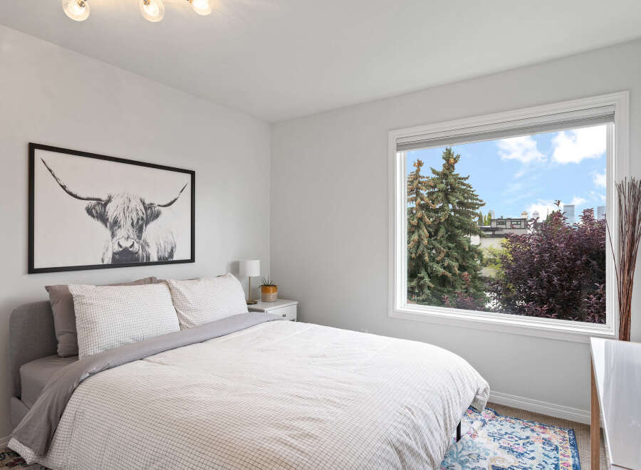 This bright bedroom features a comfortable bed with a stylish black and white Highland cow print above it.