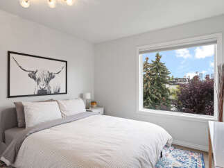 This bright bedroom features a comfortable bed with a stylish black and white Highland cow print above it.