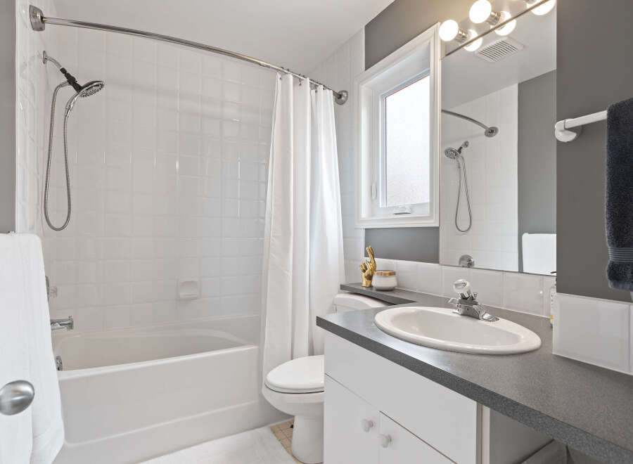 This bright and clean bathroom features a white tiled shower/tub combo with a curved shower rod and a white shower curtain.